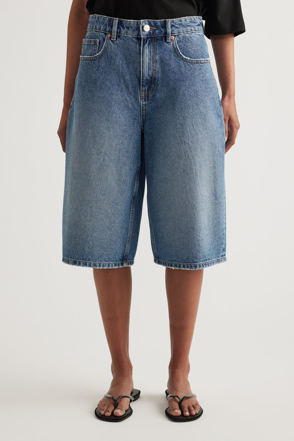 Model wearing high waisted longline blue denim shorts with a black tee and sandals