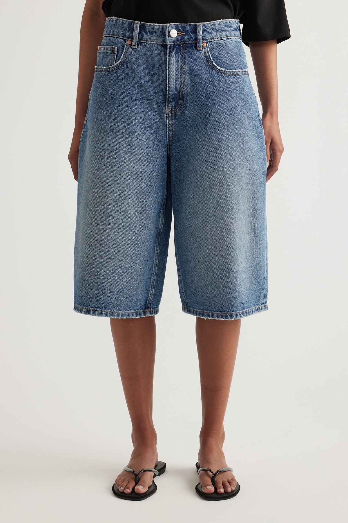Model wearing high waisted longline blue denim shorts with a black tee and sandals