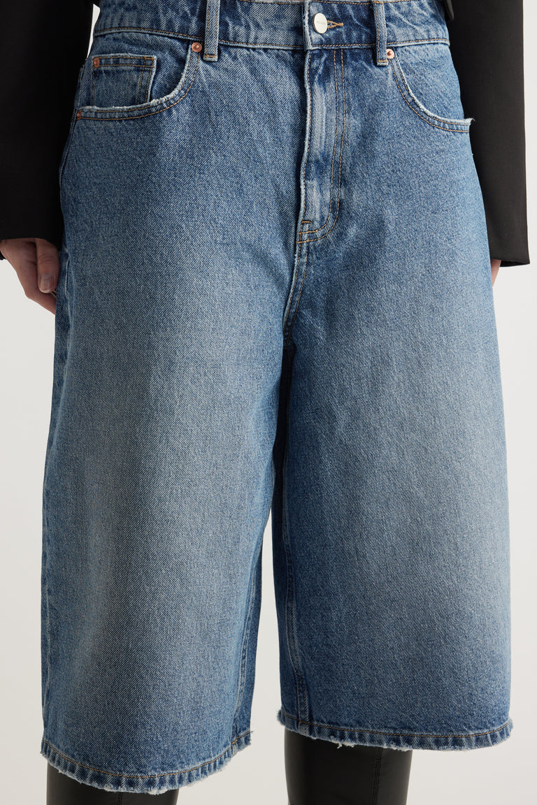 Close-up of a woman wearing high-waisted blue denim longline shorts with a straight leg cut