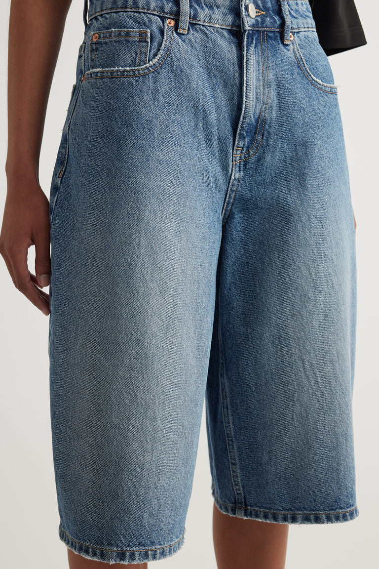 Model wearing high waisted blue denim shorts with a straight knee length fit and black top