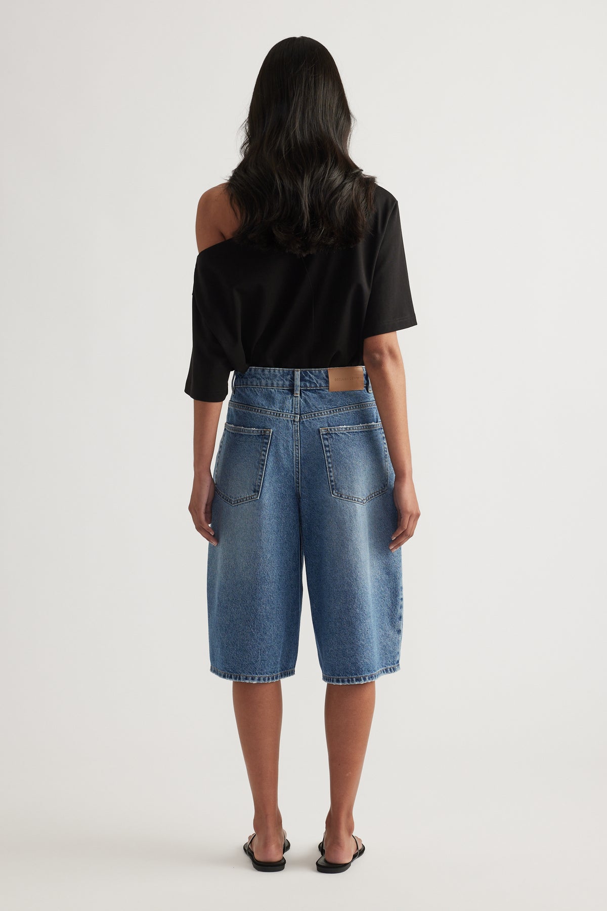 Back view of a woman wearing high waist blue denim longline shorts and a black top