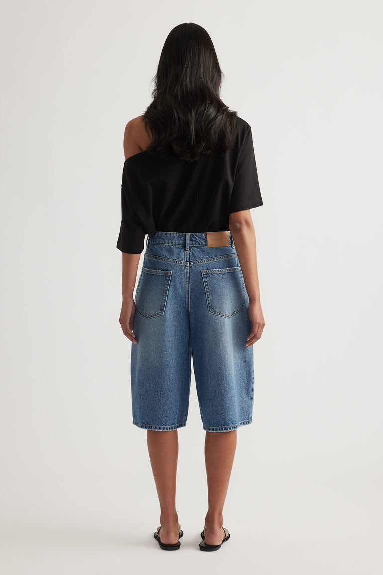 Back view of a woman wearing high waist blue denim longline shorts and a black top