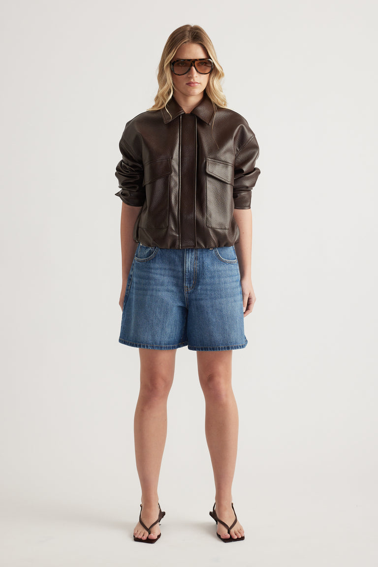 Woman wearing high rise A-line denim shorts with a brown leather jacket and black sandals