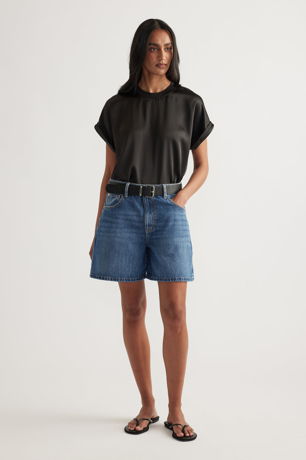 Woman wearing high-rise mid-length A-line denim shorts with a black tee and sandals