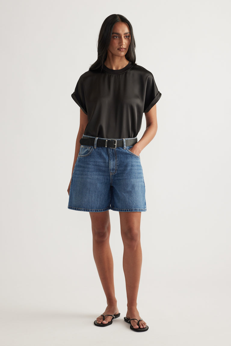 Woman wearing high-rise mid-length A-line denim shorts with a black tee and sandals
