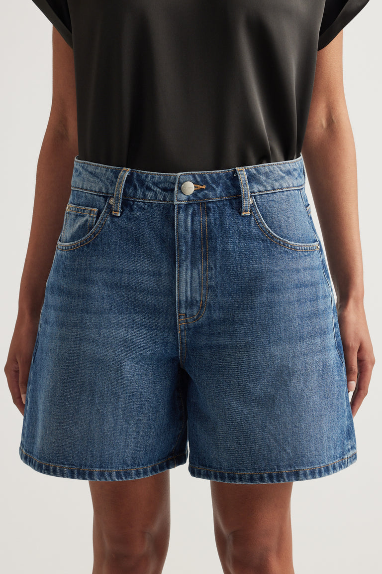 Woman wearing high-rise blue A-line denim shorts with a black top
