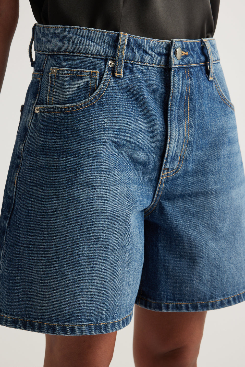Model wearing high rise blue denim A line shorts with a mid thigh length and five pocket styling