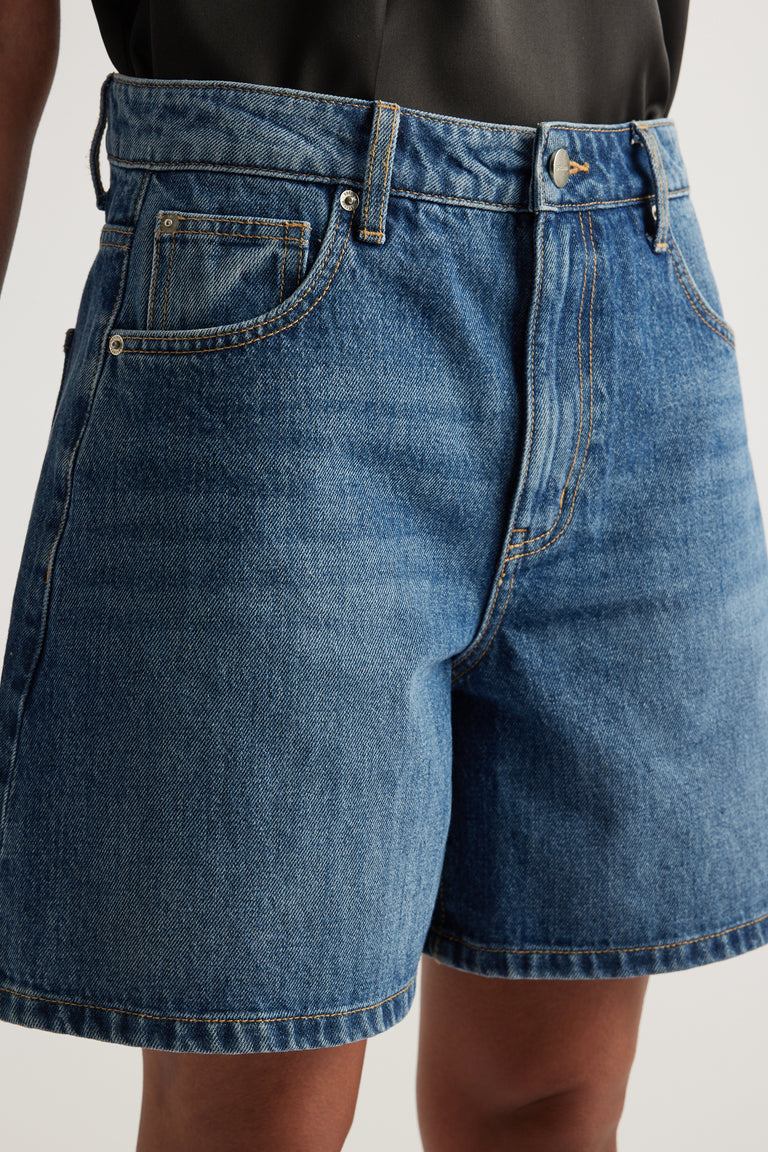 Model wearing high rise blue denim A line shorts with a mid thigh length and five pocket styling