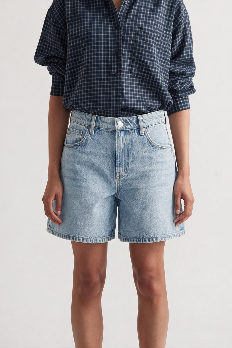 Woman wearing light wash high rise A-line denim shorts paired with a navy blue checkered long sleeve shirt