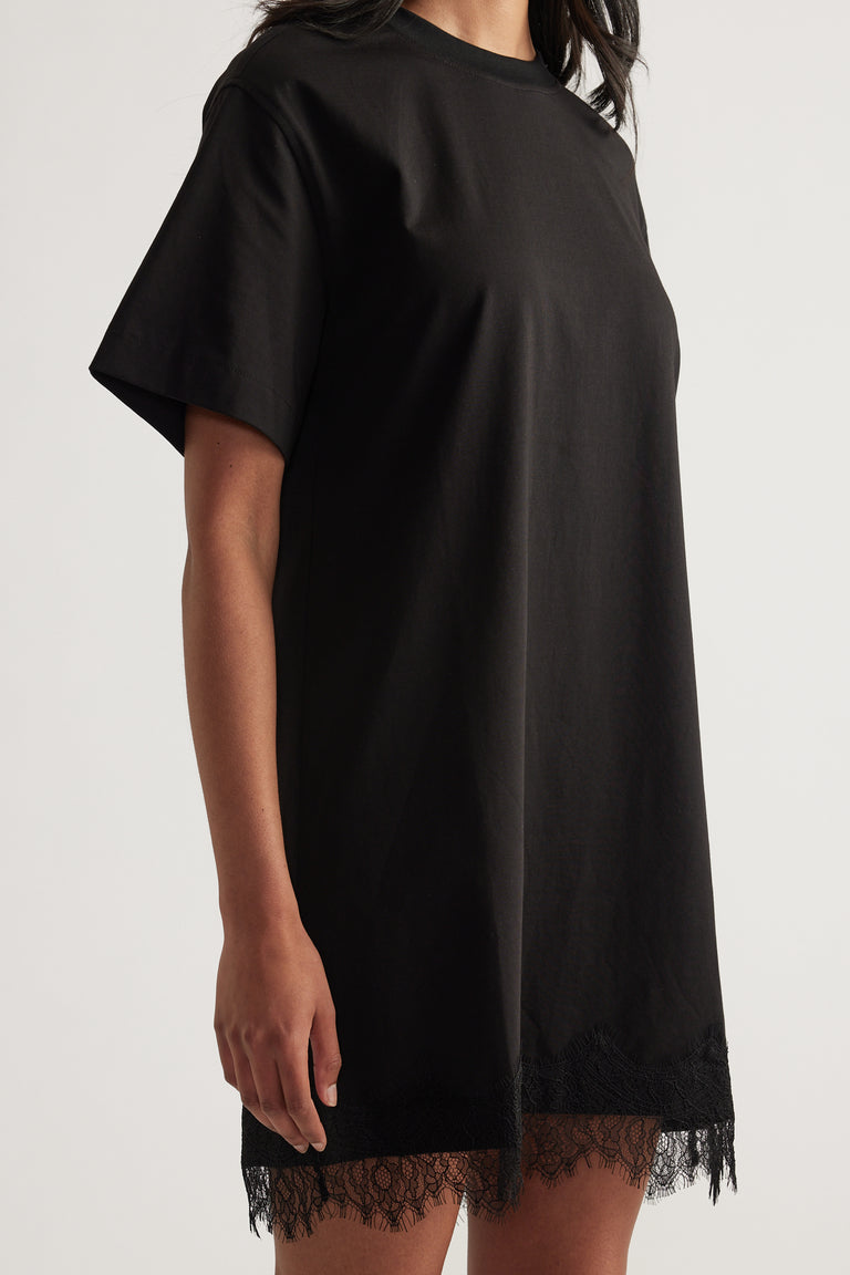 Woman wearing a black oversized mini tee dress with short sleeves and lace trim at the hem