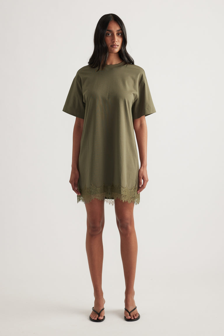 Model wearing an olive green short sleeve mini tee dress with lace trim at the hem and black sandals