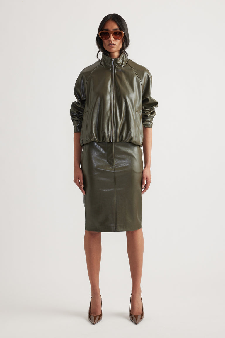 Woman wearing an olive green faux leather pencil skirt paired with a matching zip-up jacket and pointed heels