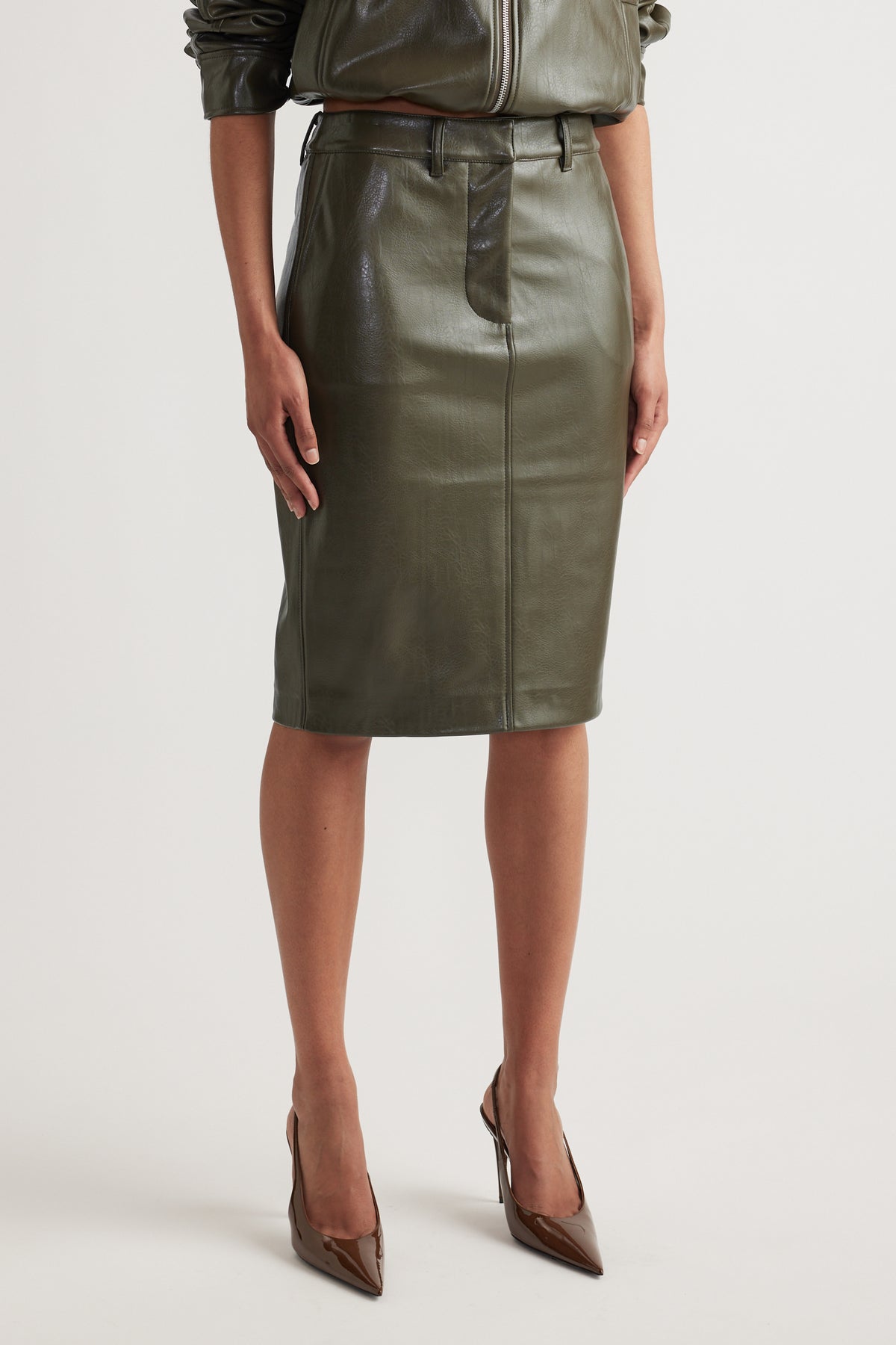 High-rise olive green faux leather pencil skirt with belt loops and straight silhouette paired with brown pointed heels