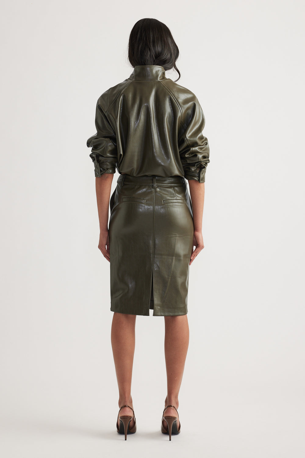 Woman wearing an olive green faux leather pencil skirt with a high waist and back slit paired with matching top and heels