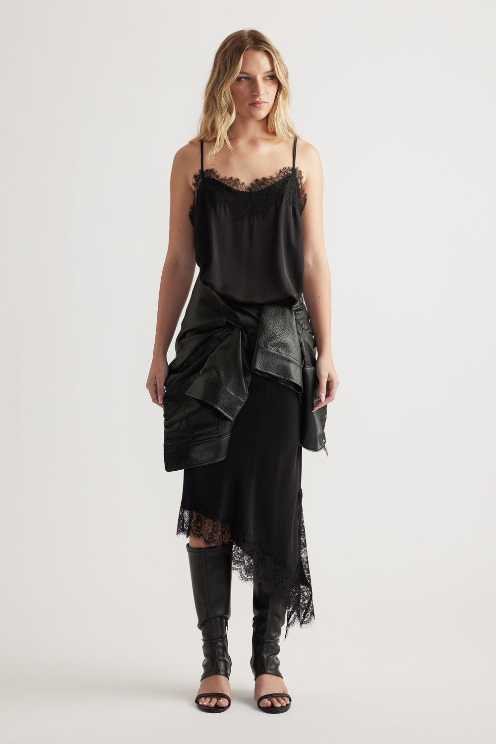 Woman wearing a black lace-trimmed cami and skirt with a leather jacket tied at the waist and knee-high boots