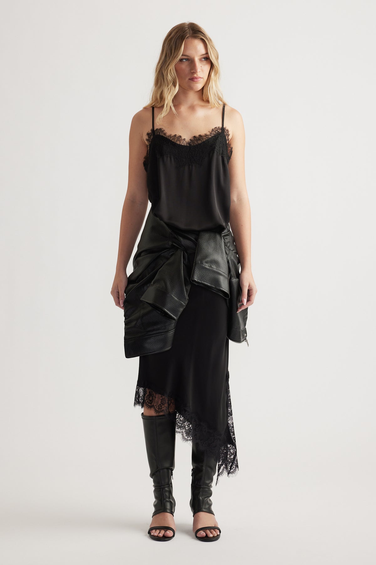 Woman wearing a black lace-trimmed cami and skirt with a leather jacket tied at the waist and knee-high boots