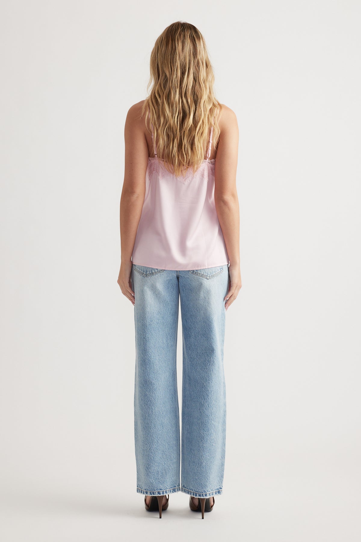 Woman seen from behind wearing light pink lace-trimmed cami and relaxed wide-leg blue jeans with heels