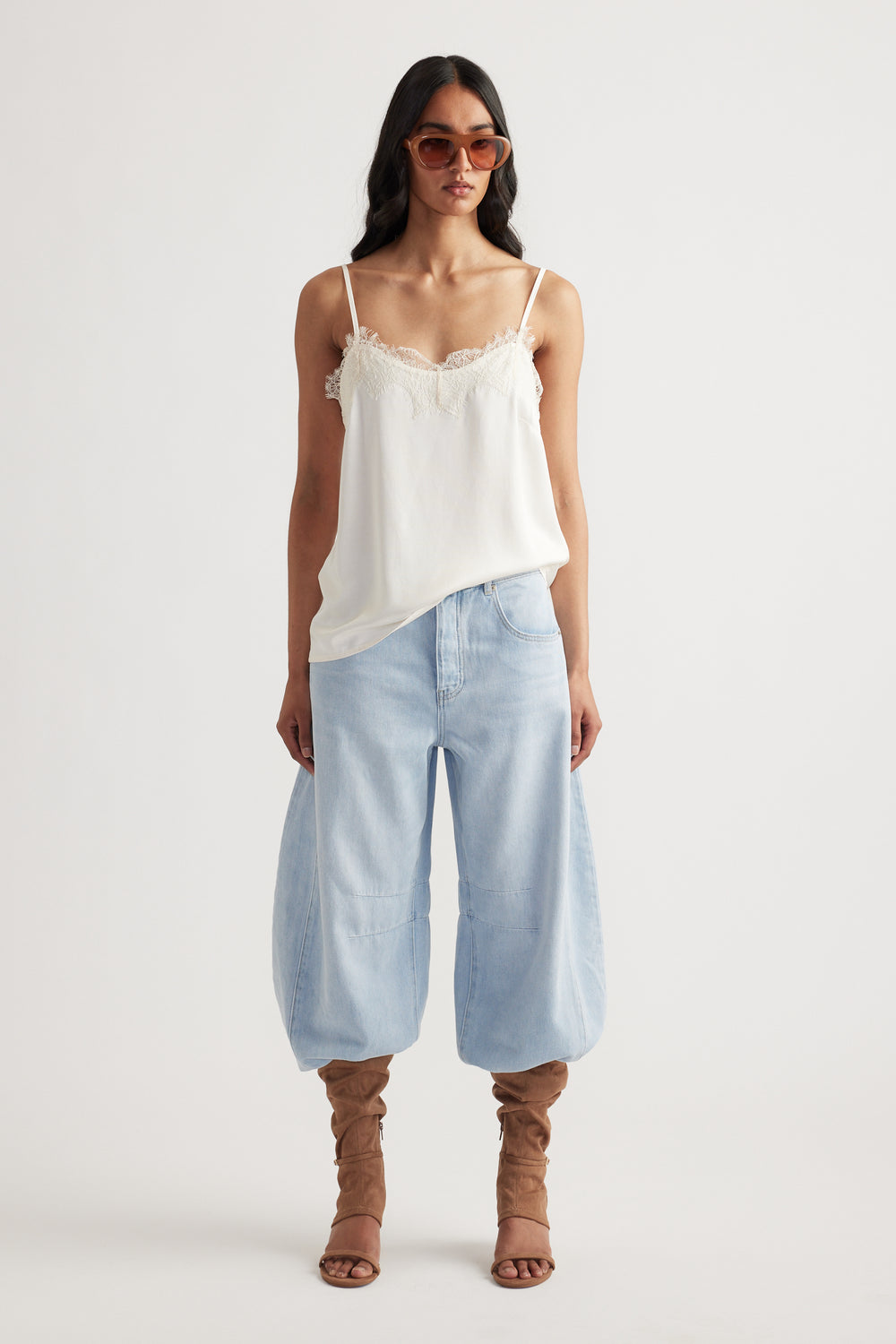 Woman wearing a white lace-trimmed cami paired with loose light-wash denim pants and brown slouchy boots