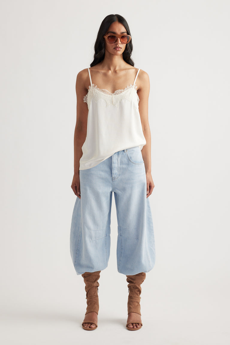 Woman wearing a white lace-trimmed cami paired with loose light-wash denim pants and brown slouchy boots