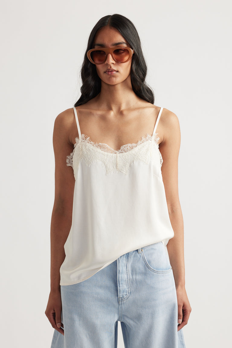 Woman wearing a delicate ivory lace-trimmed cami with thin straps paired with light blue relaxed jeans and oversized sunglasses