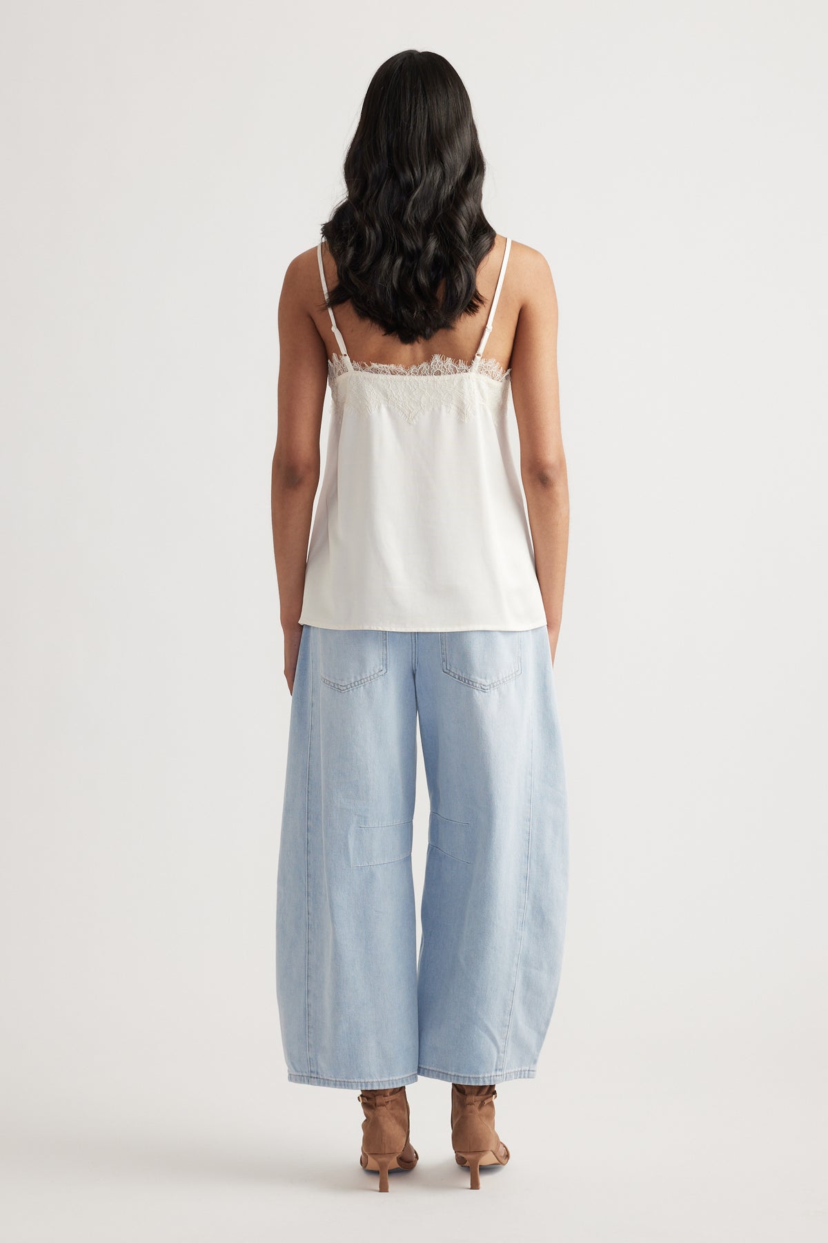 Woman wearing a cream lace-trimmed cami with adjustable straps paired with light blue wide-leg denim jeans and heeled sandals