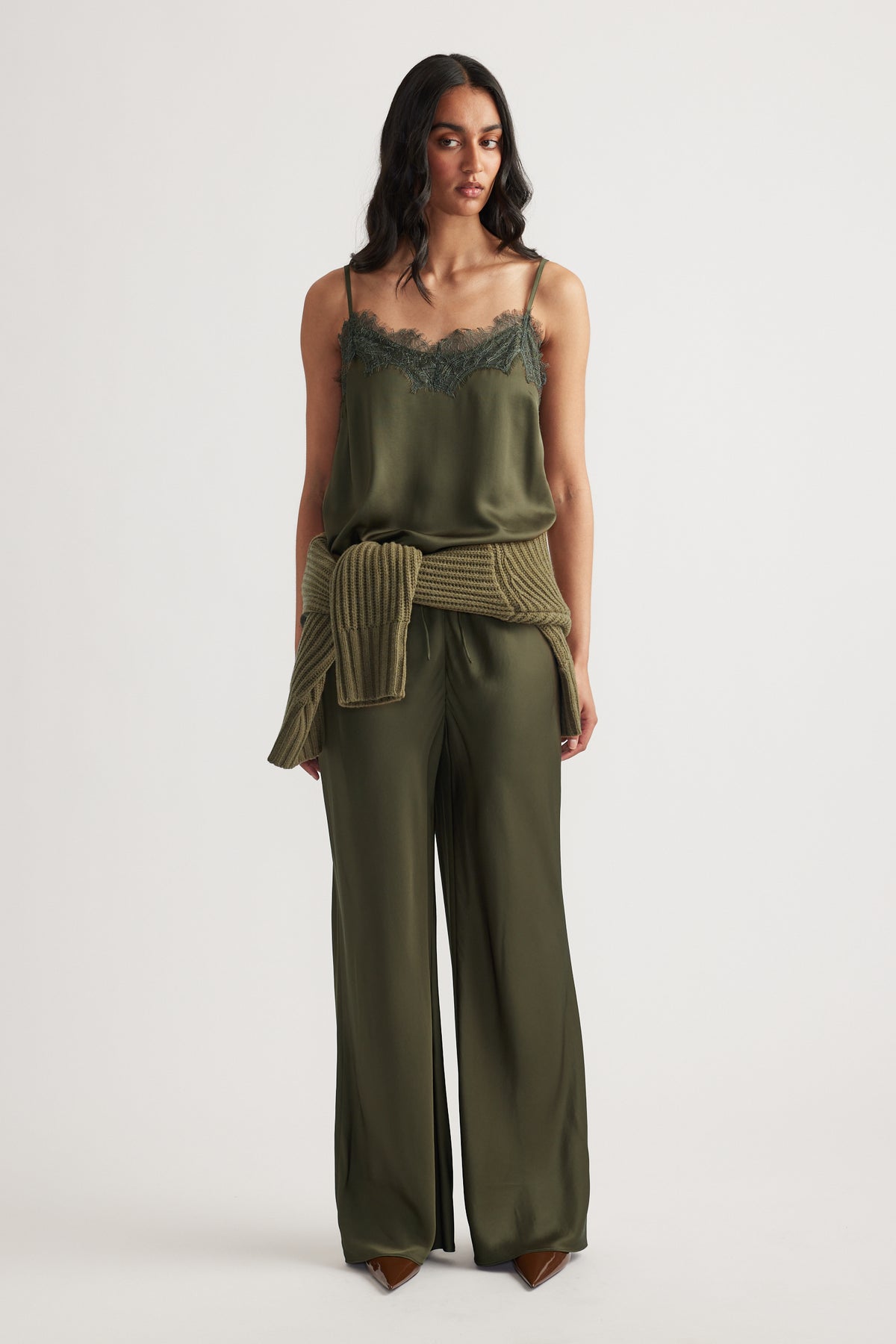 Woman wearing a dark olive lace-trimmed cami paired with matching wide-leg pants and a ribbed sweater tied at the waist