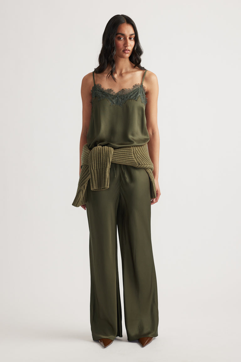 Woman wearing a dark olive lace-trimmed cami paired with matching wide-leg pants and a ribbed sweater tied at the waist