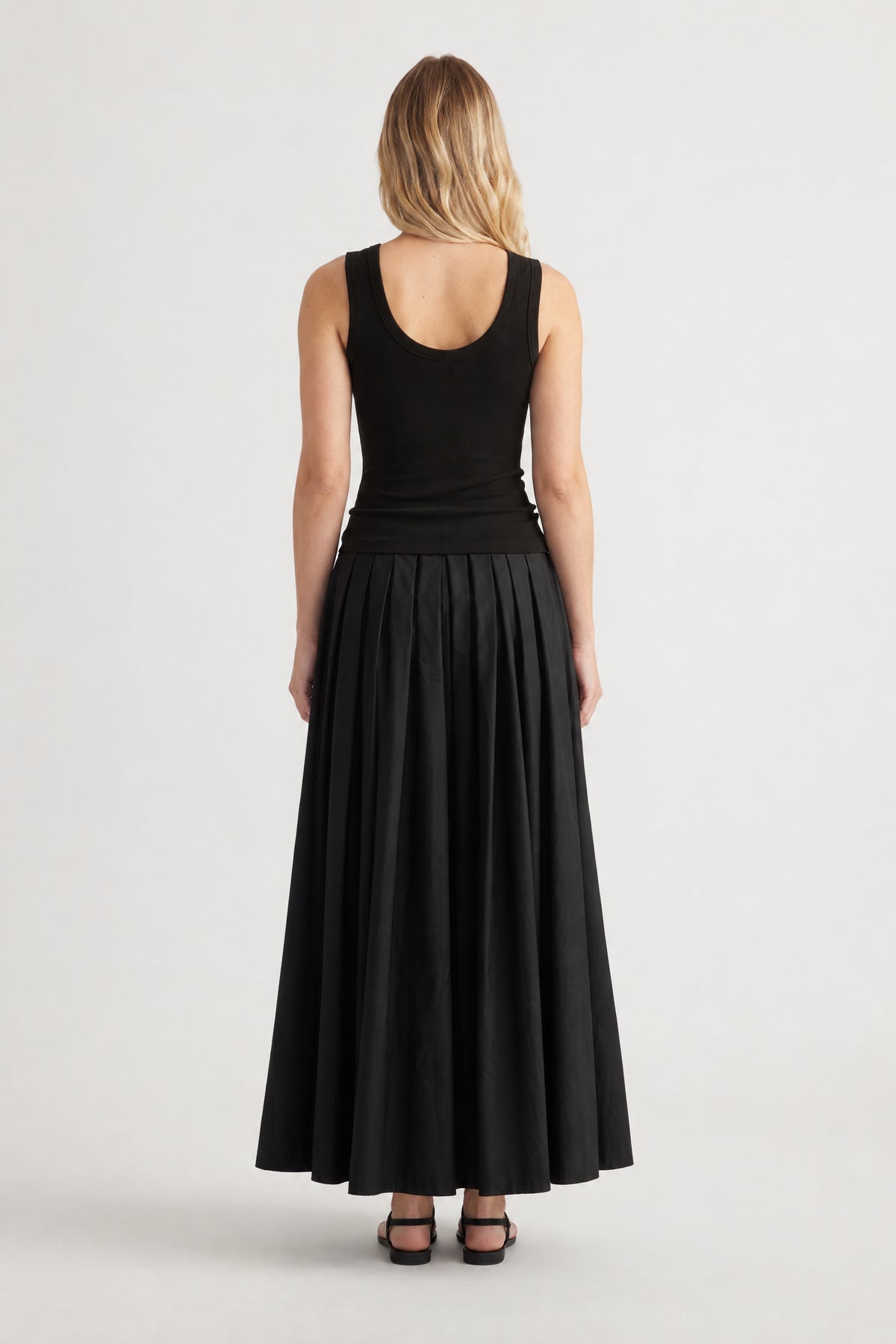 Back view of a woman wearing a black sleeveless top and long pleated skirt