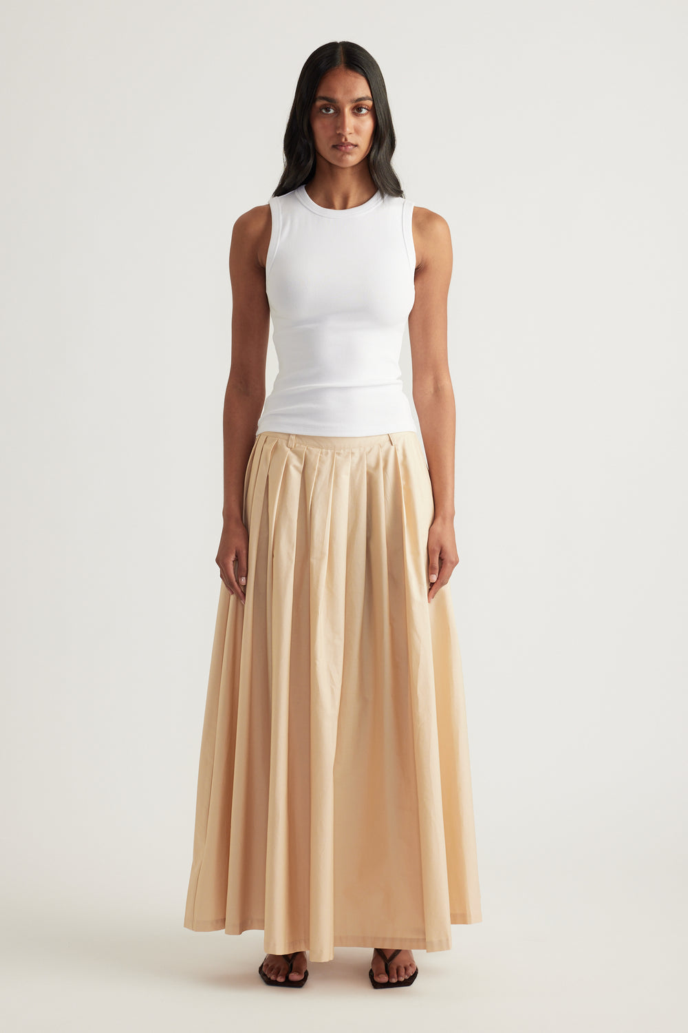 Model wearing a cream pleated ankle-length A-line skirt with a white sleeveless top