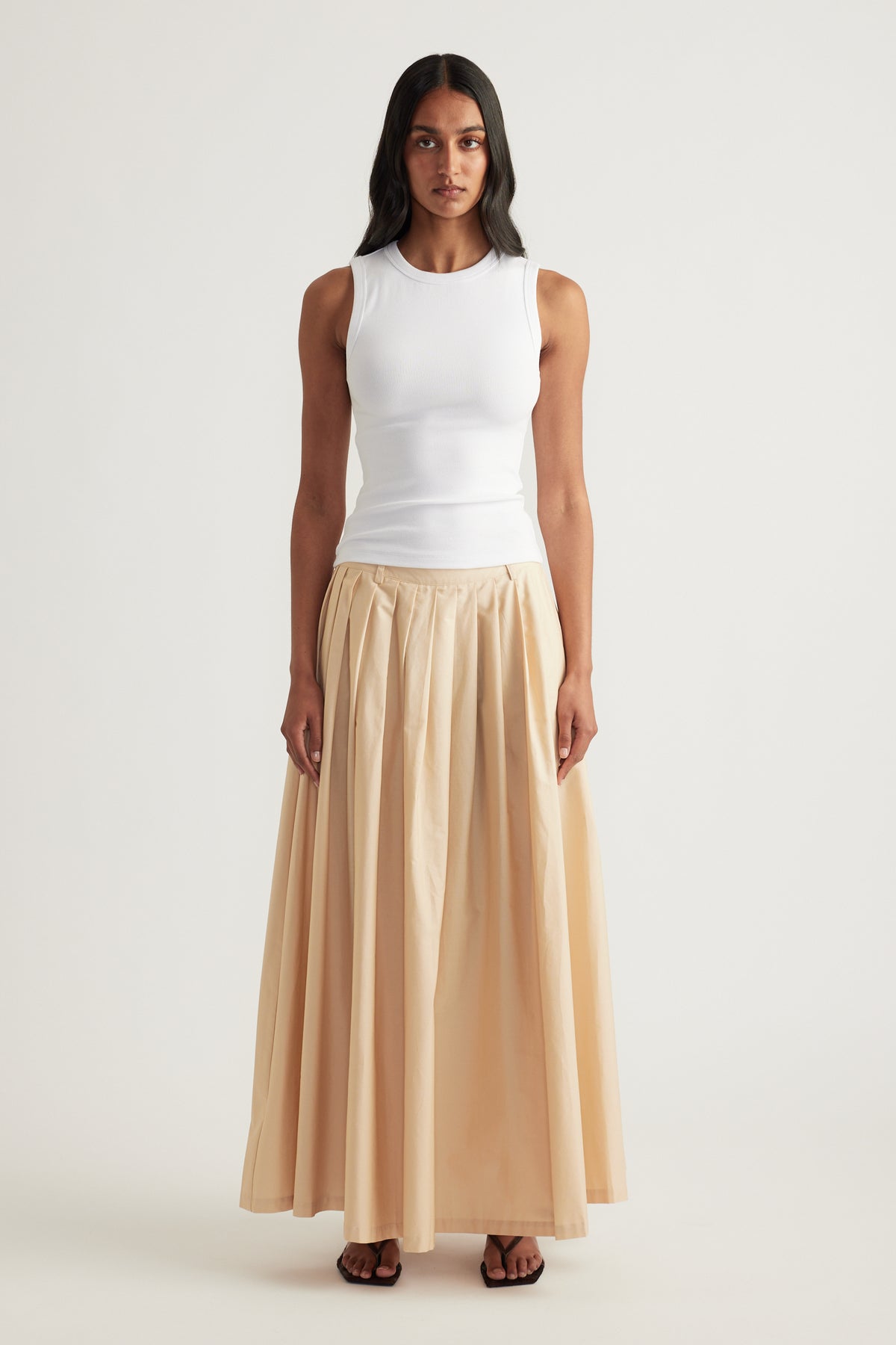 Model wearing a cream pleated ankle-length A-line skirt with a white sleeveless top