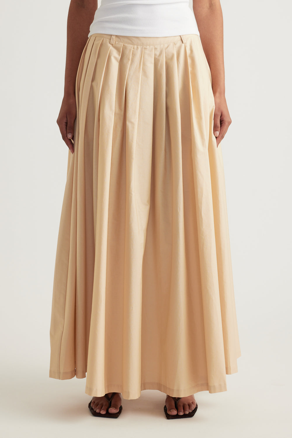 Woman wearing a cream pleated ankle-length skirt with a white top and black sandals