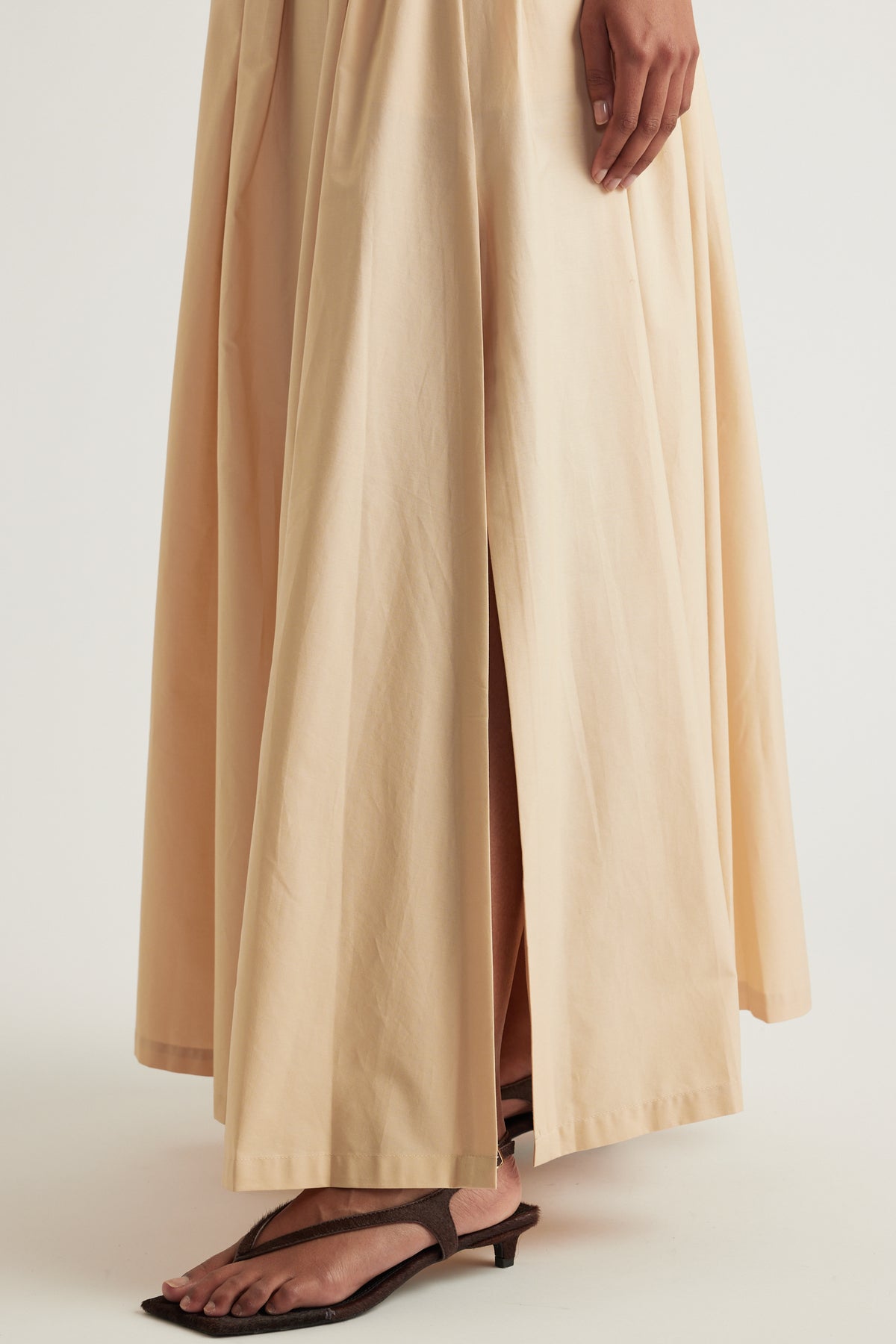 Beige pleated ankle-length skirt styled with flat sandals