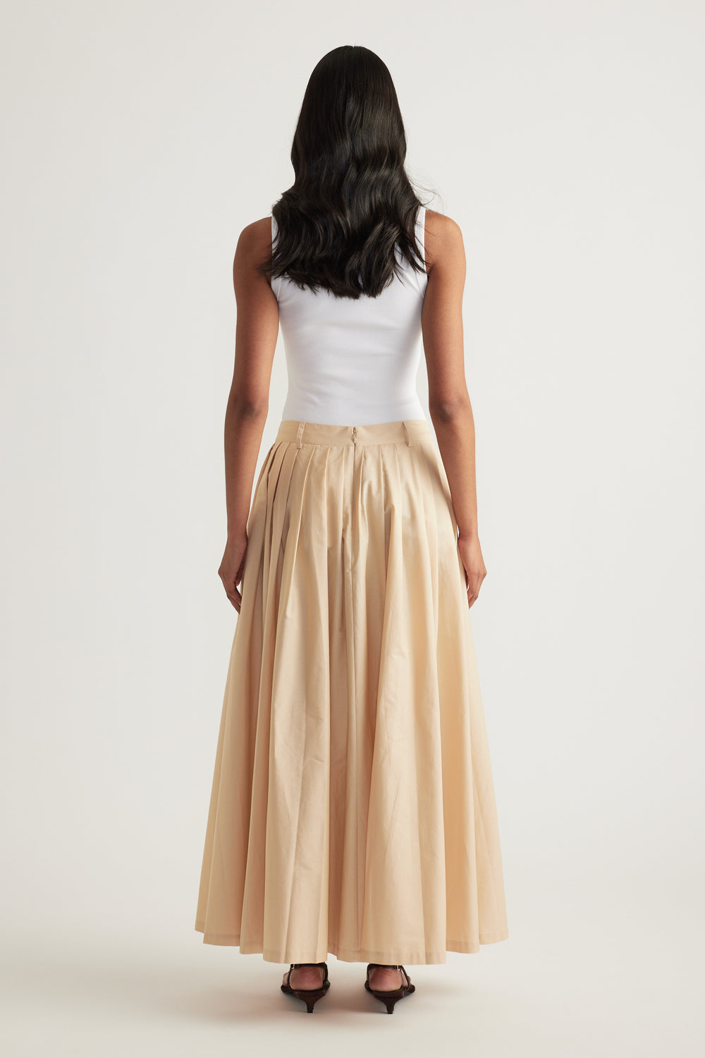 Model wearing a beige pleated ankle length skirt with a white sleeveless top and heels