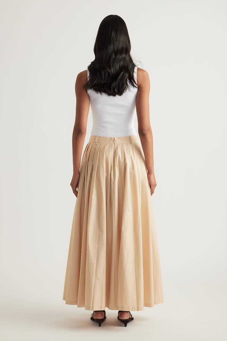 Model wearing a beige pleated ankle length skirt with a white sleeveless top and heels