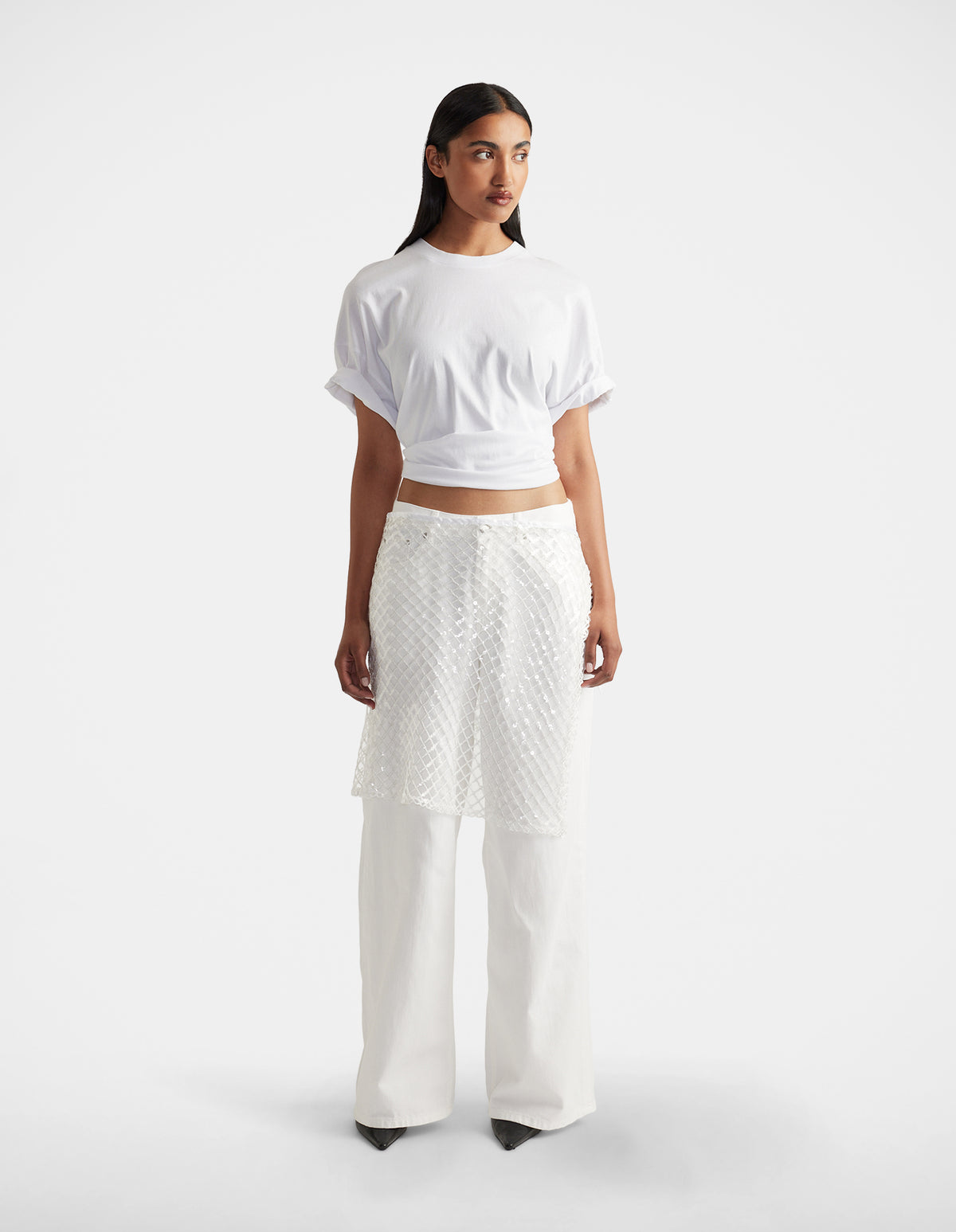 Woman wearing a white short-sleeve top paired with textured white layered pants and black pointed shoes
