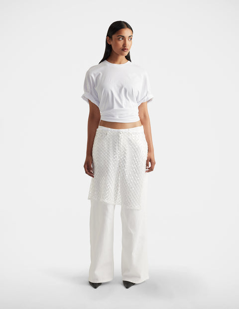 Woman wearing a white short-sleeve top paired with textured white layered pants and black pointed shoes