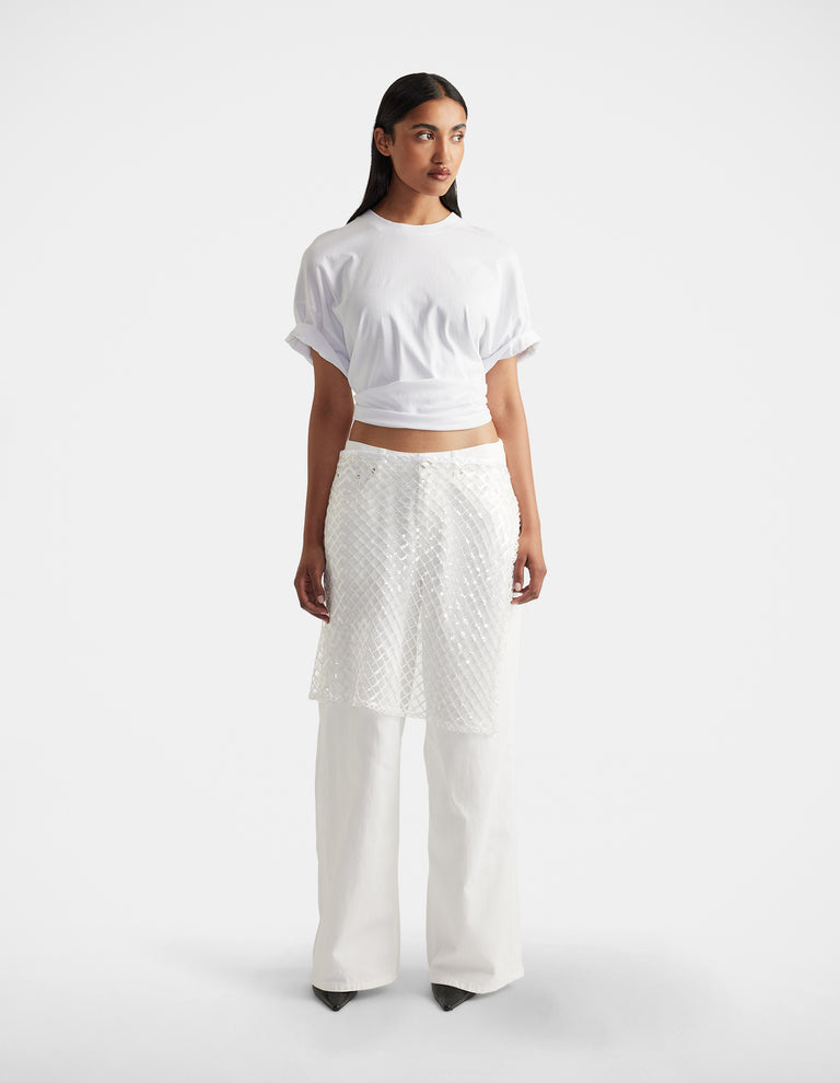 Woman wearing a white short-sleeve top paired with textured white layered pants and black pointed shoes