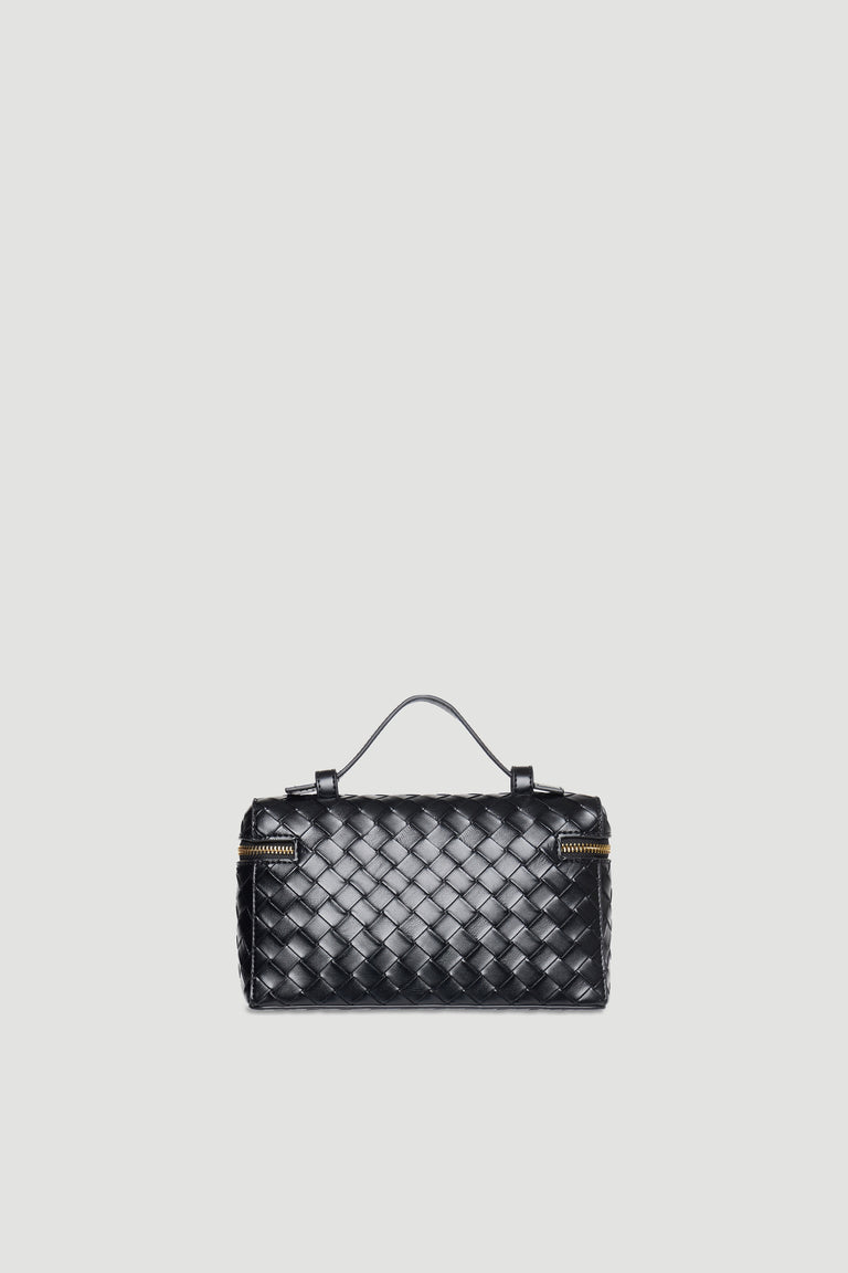 Black woven vanity-style bag with top handle, brass zipper accents, and detachable shoulder strap against light background