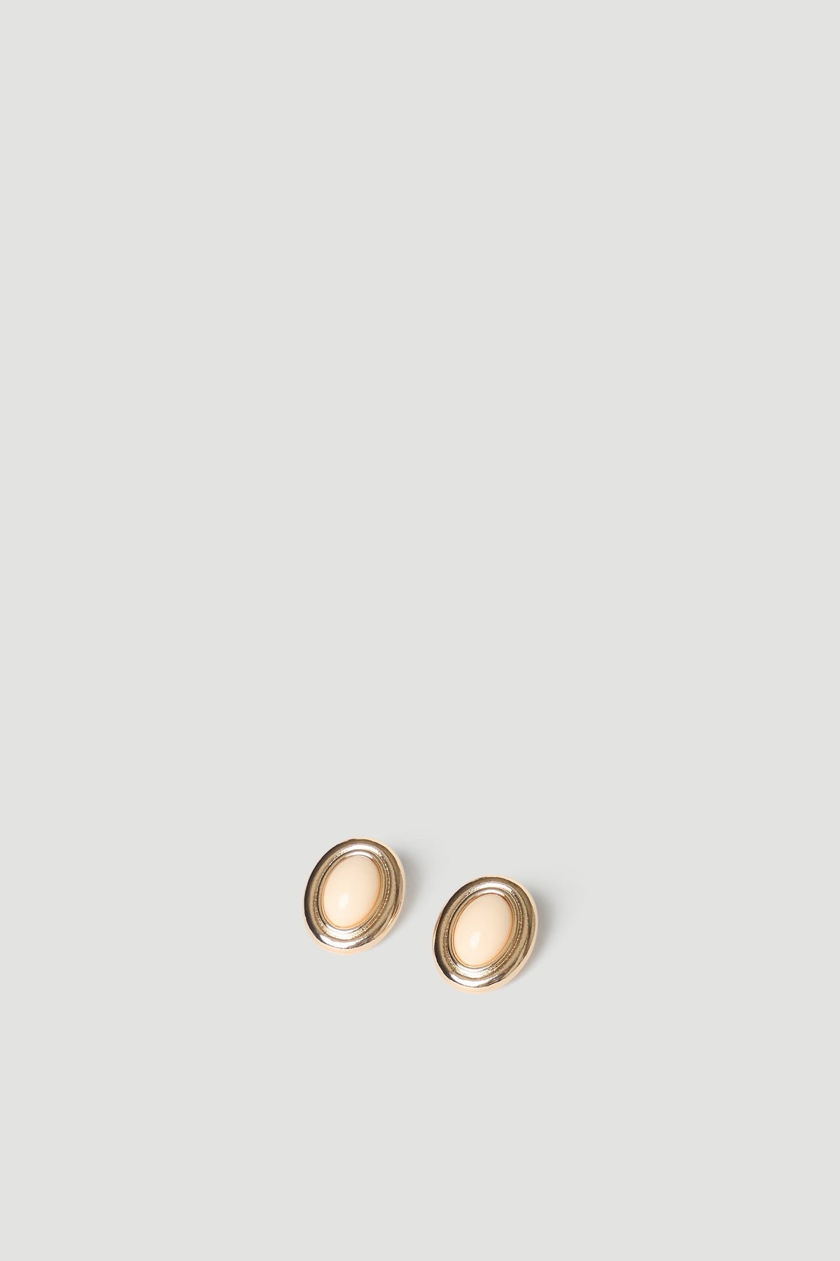 Pair of oval gold stud earrings with cream-colored center stone set against a neutral background.