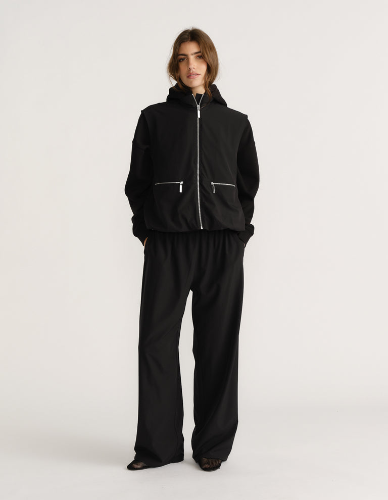 Woman wearing relaxed wide-leg black pull-on pants paired with a casual black zip-up jacket with pockets