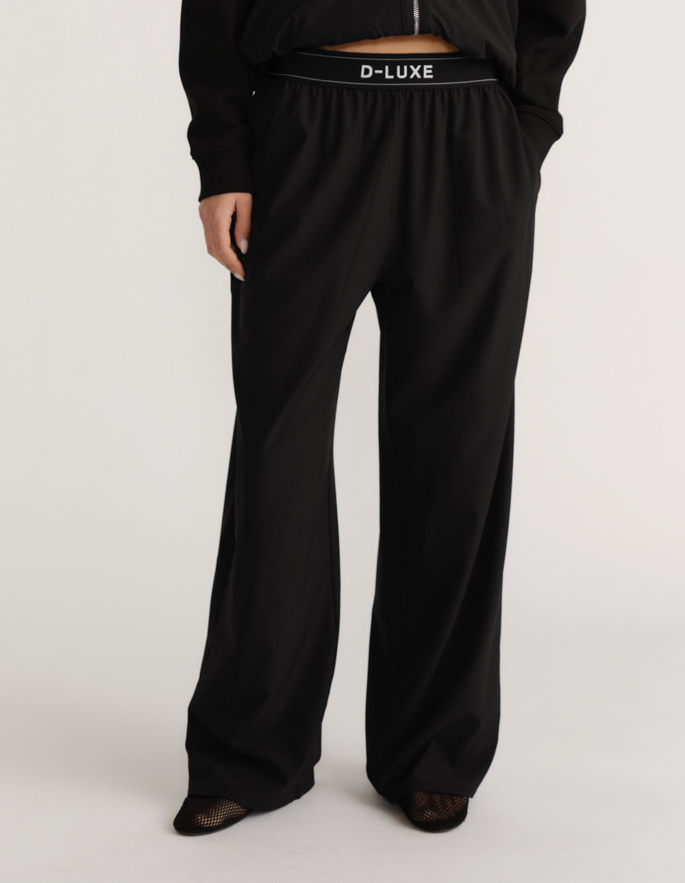 Woman wearing high-rise wide-leg black pull-on pants with elastic waistband and logo detail at waist