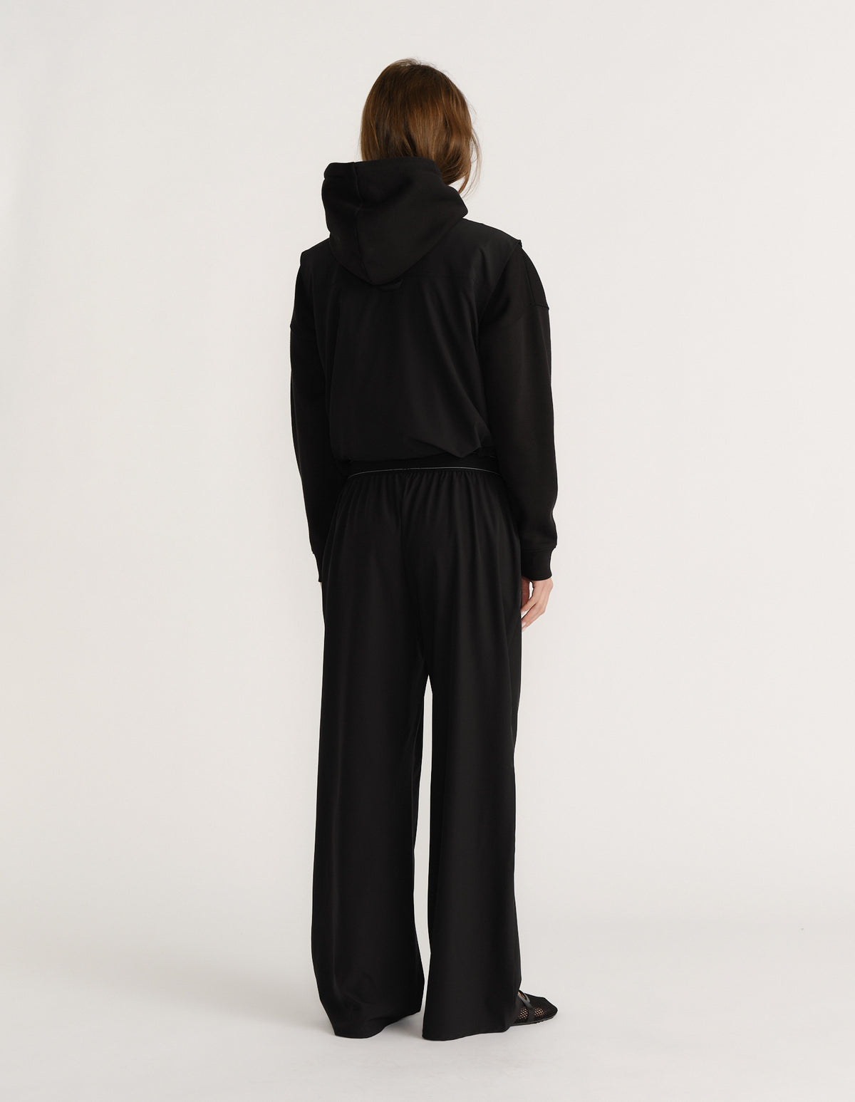 Woman wearing black wide-leg pants with elasticated waist paired with black hooded top viewed from behind