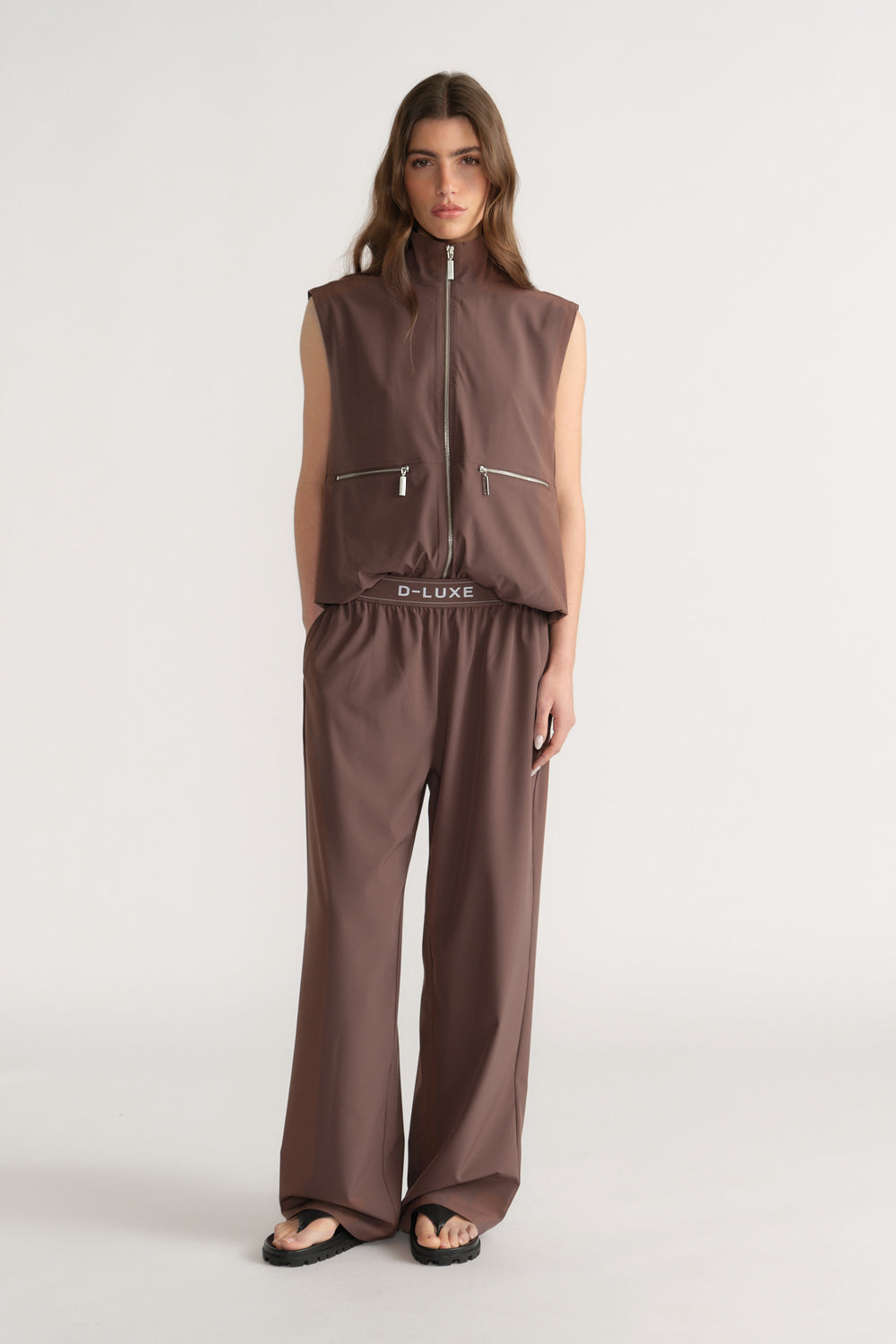 Woman wearing brown wide-leg pants with a matching zip-front gilet and black sandals
