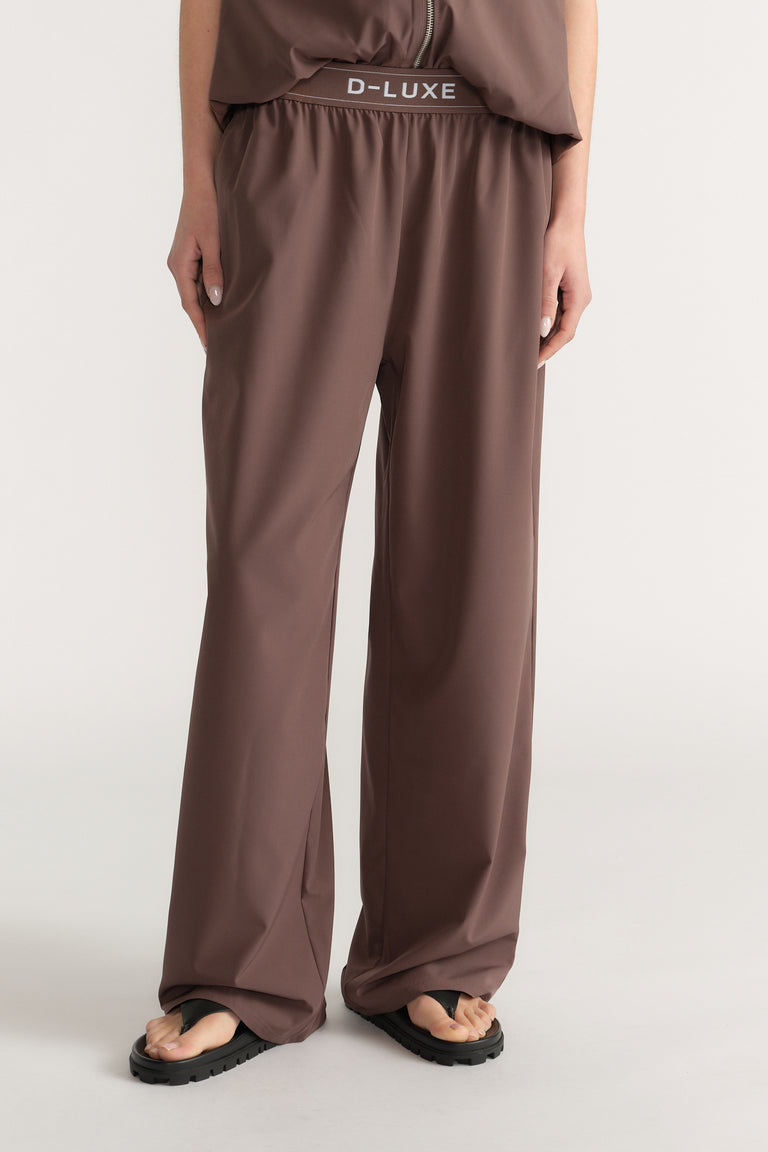 Woman wearing brown D-Luxe high-rise wide-leg pull-on pants with an elasticated waist and flat sandals