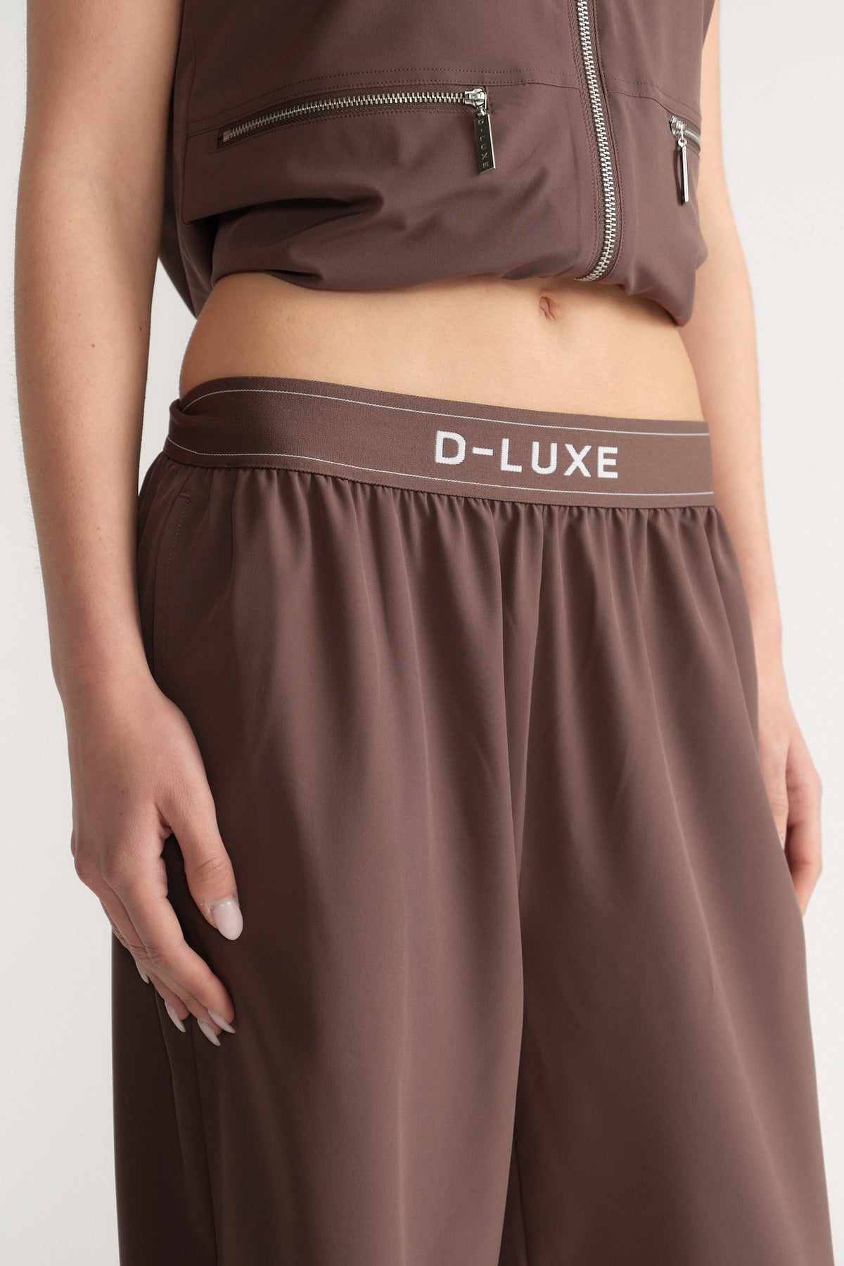 Model wearing brown wide-leg pants with an elastic D-Luxe waistband and matching utility vest