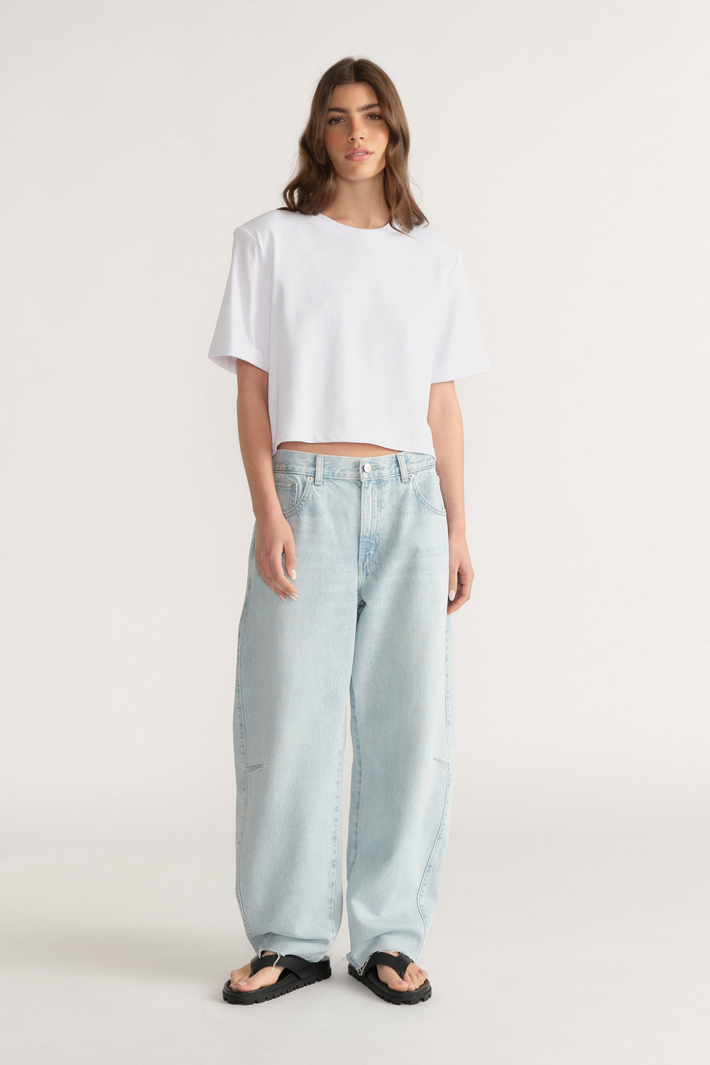 Woman wearing relaxed fit light blue jeans with wide legs paired with a loose white crop top and black sandals
