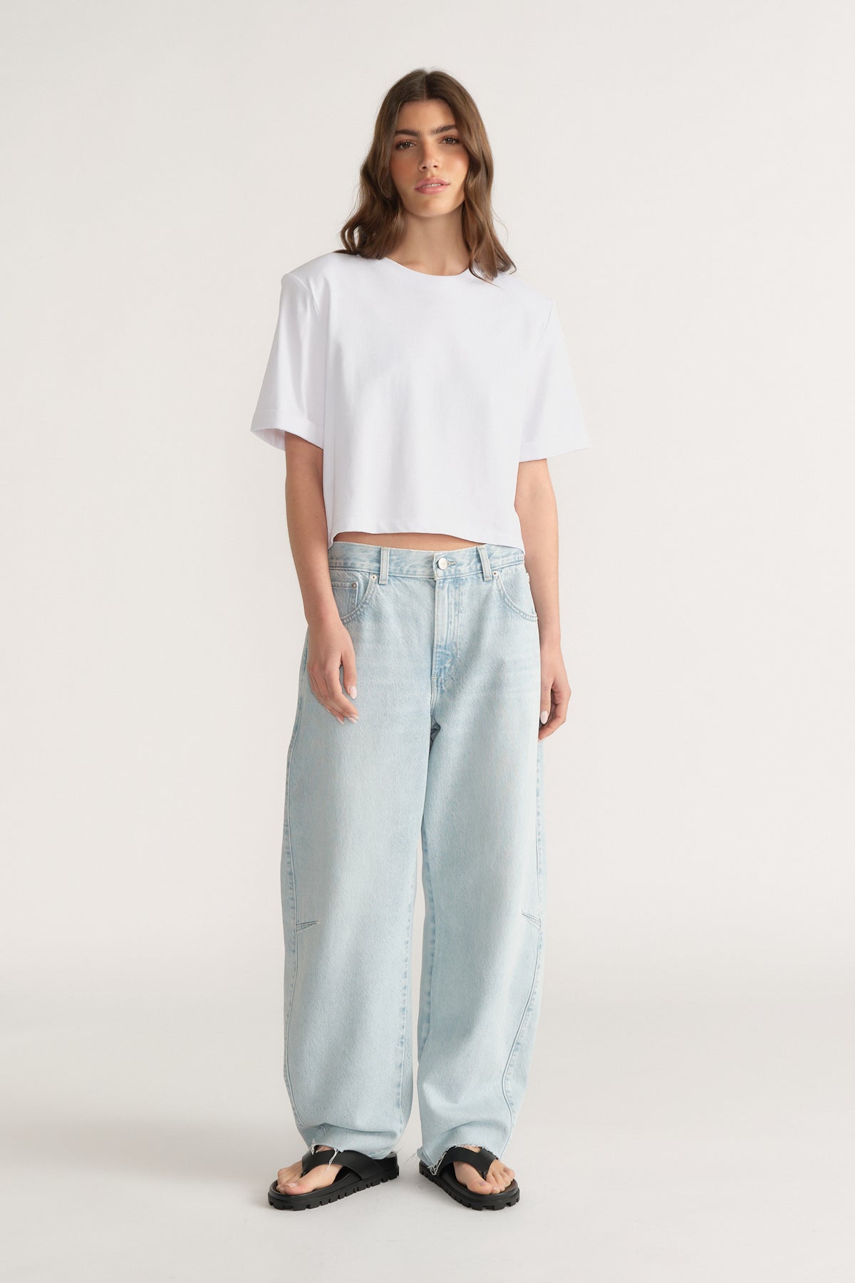 Woman wearing relaxed fit light blue jeans with wide legs paired with a loose white crop top and black sandals