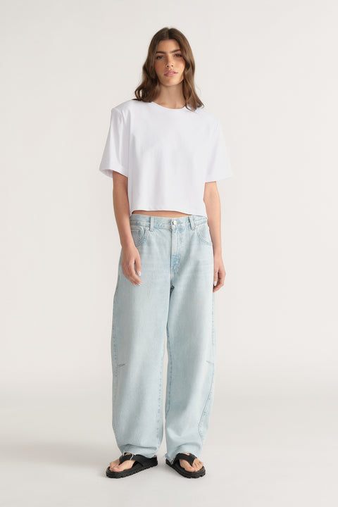 Woman wearing relaxed fit light blue jeans with wide legs paired with a loose white crop top and black sandals