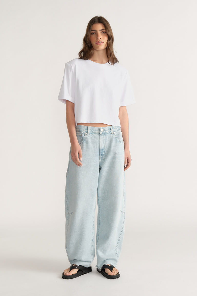 Woman wearing relaxed fit light blue jeans with wide legs paired with a loose white crop top and black sandals