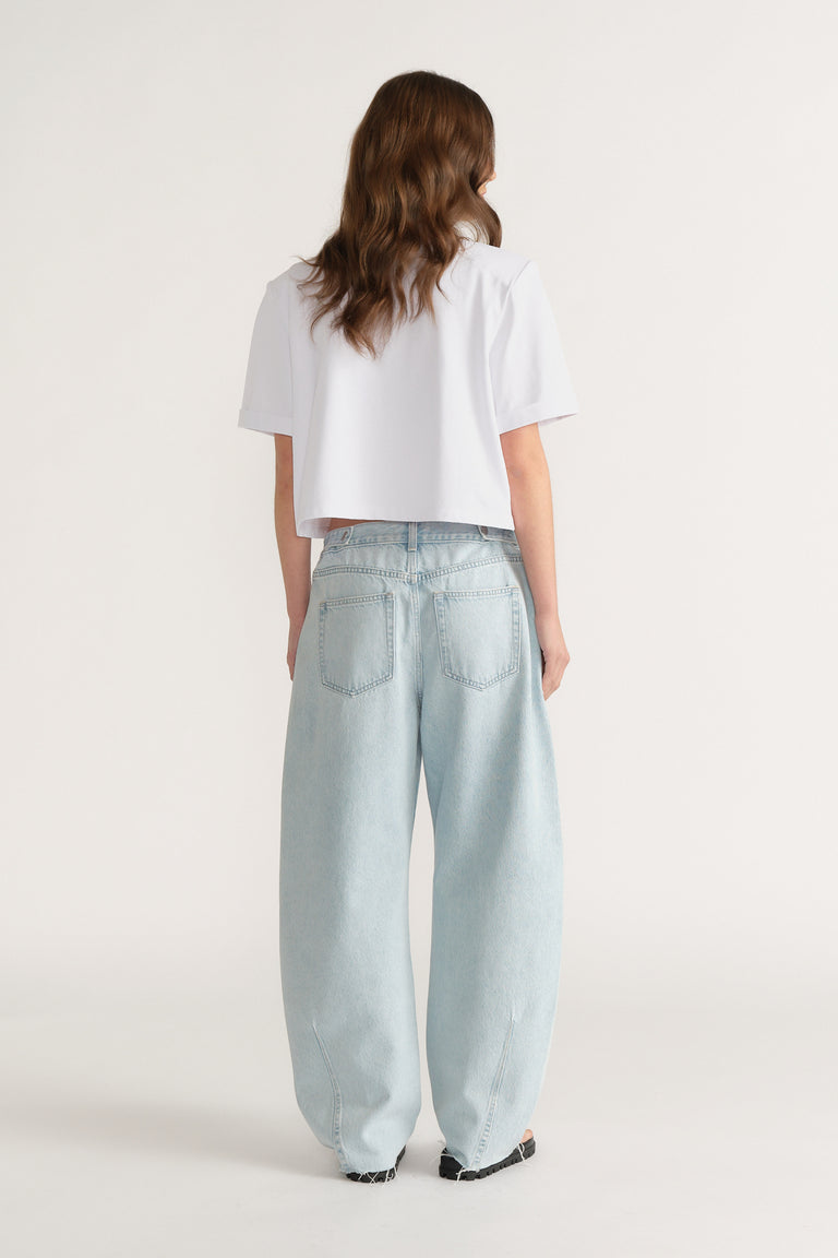 Rear view of woman wearing light blue wide-leg jeans with a cropped white short sleeve top and black shoes